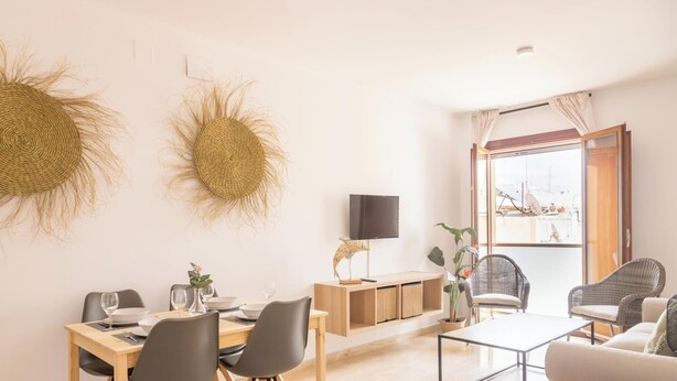 A modern living room with a dining area, wicker wall decor, a flat-screen TV, wicker chairs, and a view through a large window. - Casa Capuchinos - FREE PARKING by Cadiz Time (Cádiz)