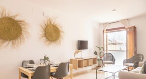 Ein modernes Wohnzimmer mit Essbereich, Wanddekoration aus Weidwerk, einem Flachbildfernseher, Weidenstühle und Blick durch ein großes Fenster.