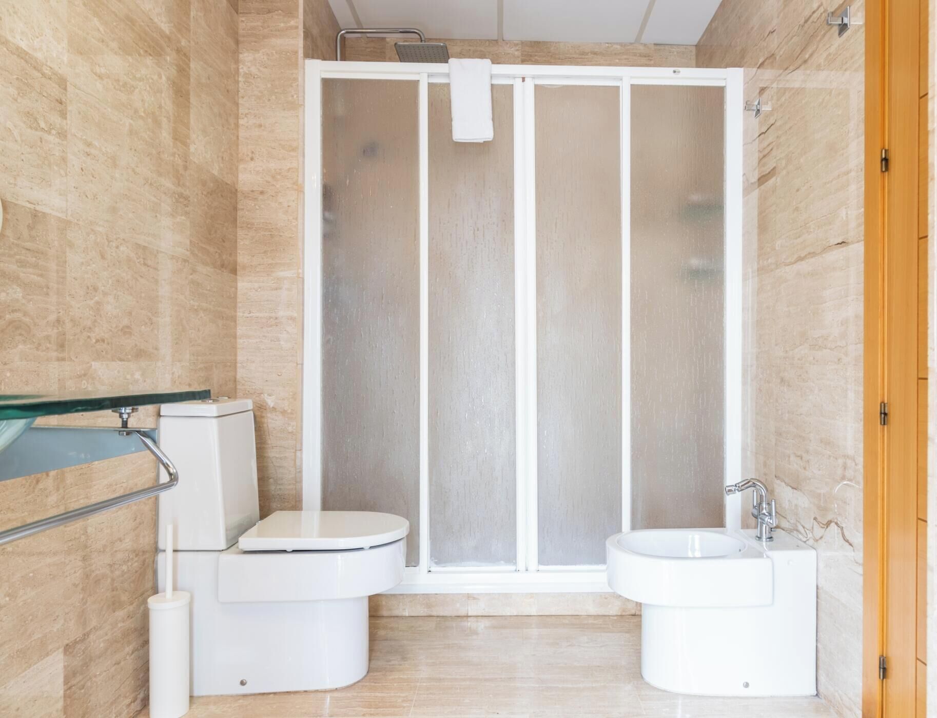 A bathroom with a shower enclosure, two toilets, a sink, and a glass shower door.