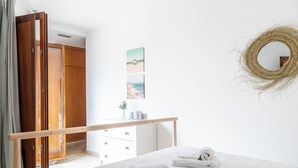A bedroom with a wooden door, a white dresser, a bed with rolled towels, a wooden bench, and a wall-mounted mirror. - Casa Capuchinos - FREE PARKING by Cadiz Time (Cádiz)