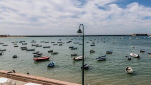 A coastal scene with numerous boats anchored in calm waters, a clear sky, and a distant stone structure. - Casa Capuchinos - FREE PARKING by Cadiz Time (Cádiz)