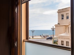 Une vue depuis une fenêtre donnant sur une rue côtière, avec des bâtiments et un ciel dégagé.