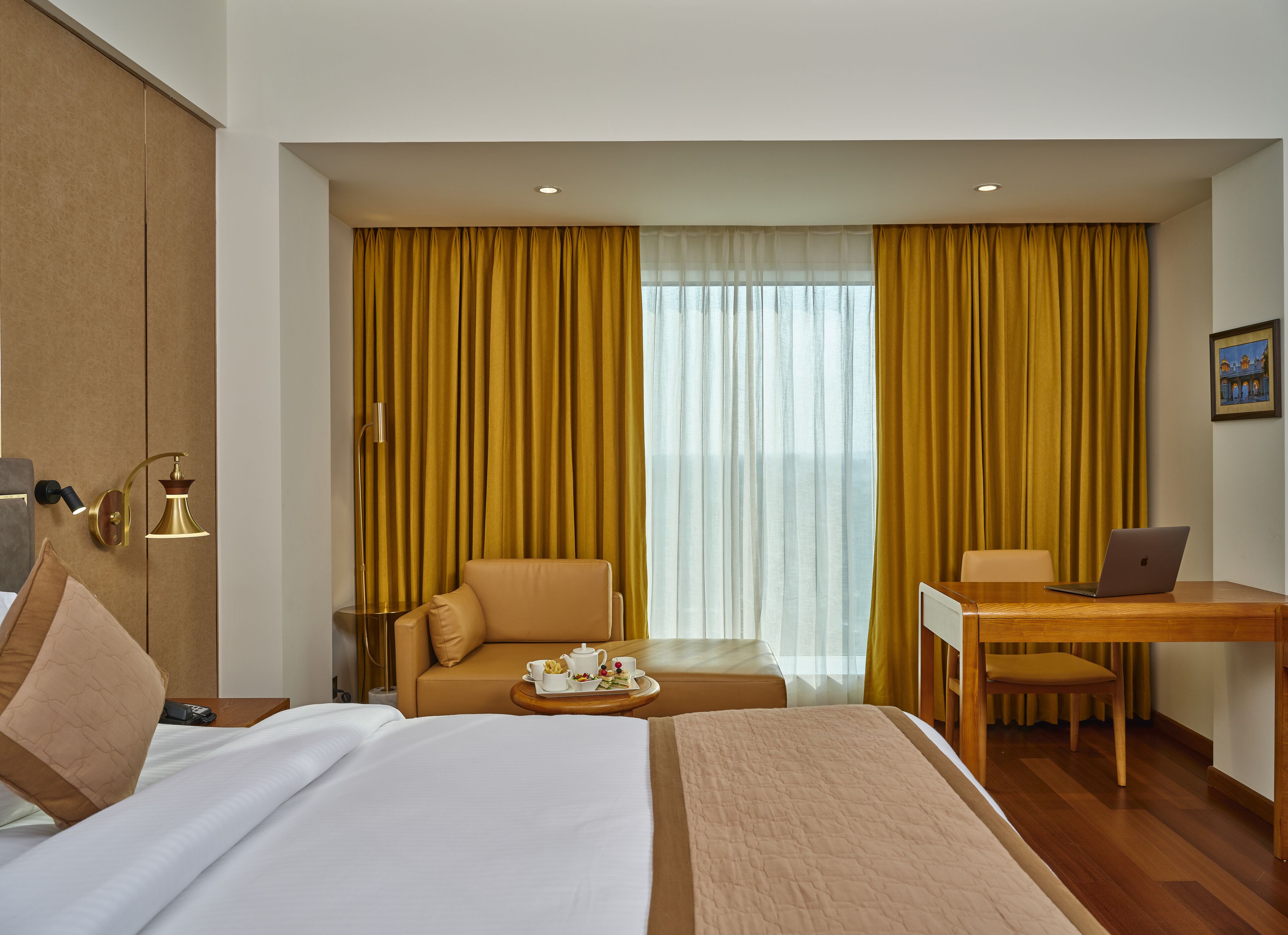 Een hotelkamer met een bed, een bureau met een laptop, een stoel, een bank en gordijnen.