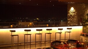 Un área de bar con seis taburetes, una pared de piedra y vista a la ciudad de noche.