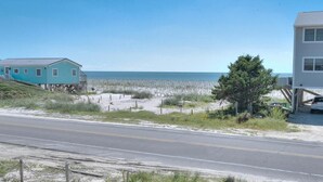 Eine Küstenstraße mit einem türkisfarbenen Haus und einem weißen Gebäude, die zu einem Strand mit wenig Vegetation führt.