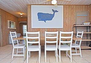 A dining area with a wooden wall, a framed artwork of a blue whale, and white chairs with a table.