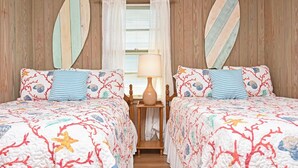 Ein Zimmer mit zwei Betten, einem Nachttisch, einer Lampe und zwei an der Wand befestigten Surfbrettern.