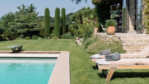 A poolside area with a lounge chair, a small table, and a stone wall with a potted plant. - Heated pool, Outdoor cinema, Spa Terrace, Stroll to Shops, luxury equipped (Mougins)