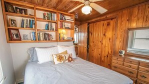 A bedroom with a bed, a wooden bookshelf, a dresser, and a ceiling fan. - Experience oceanfront bliss at The Captain's Quarters, Holden Beach! (Holden Beach)