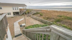 A beach house with a wooden deck, a covered porch, and a staircase leading to a deck area. - Experience oceanfront bliss at The Captain's Quarters, Holden Beach! (Holden Beach)