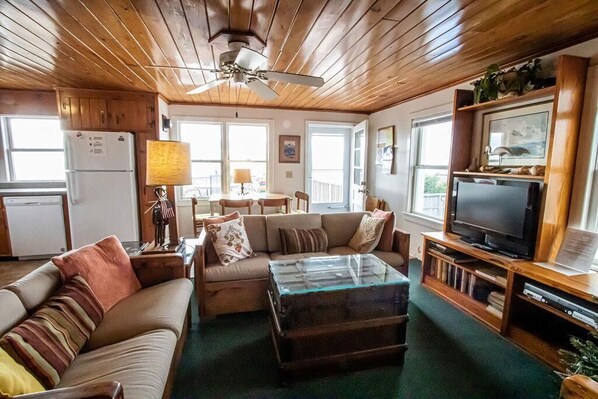 A cozy living room with a wooden ceiling, a glass coffee table, a sofa, and a television on a wooden stand.