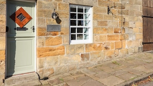 A stone building with a white door, a small window, and a metal sign reading "Michaelmas Cottage 2". - Michaelmass Cottage (Whitby)