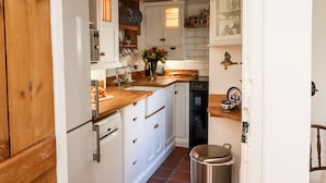 A compact kitchen with white cabinets, a wooden countertop, a stainless steel trash bin, and a built-in oven. - Michaelmass Cottage (Whitby)