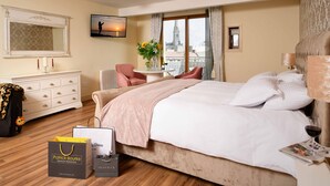 Habitación de hotel con una cama grande, un escritorio con silla, una tocador con cajones, un espejo y una ventana con vistas a una torre.