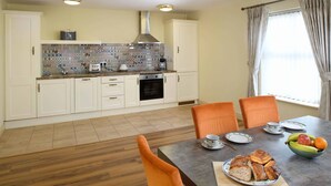 Una cocina moderna con armarios blancos, salpicadero de azulejos y un comedor con mesa lista para el desayuno.