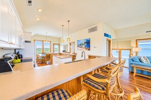 A spacious kitchen with a large island, wooden chairs, and a view of the ocean.