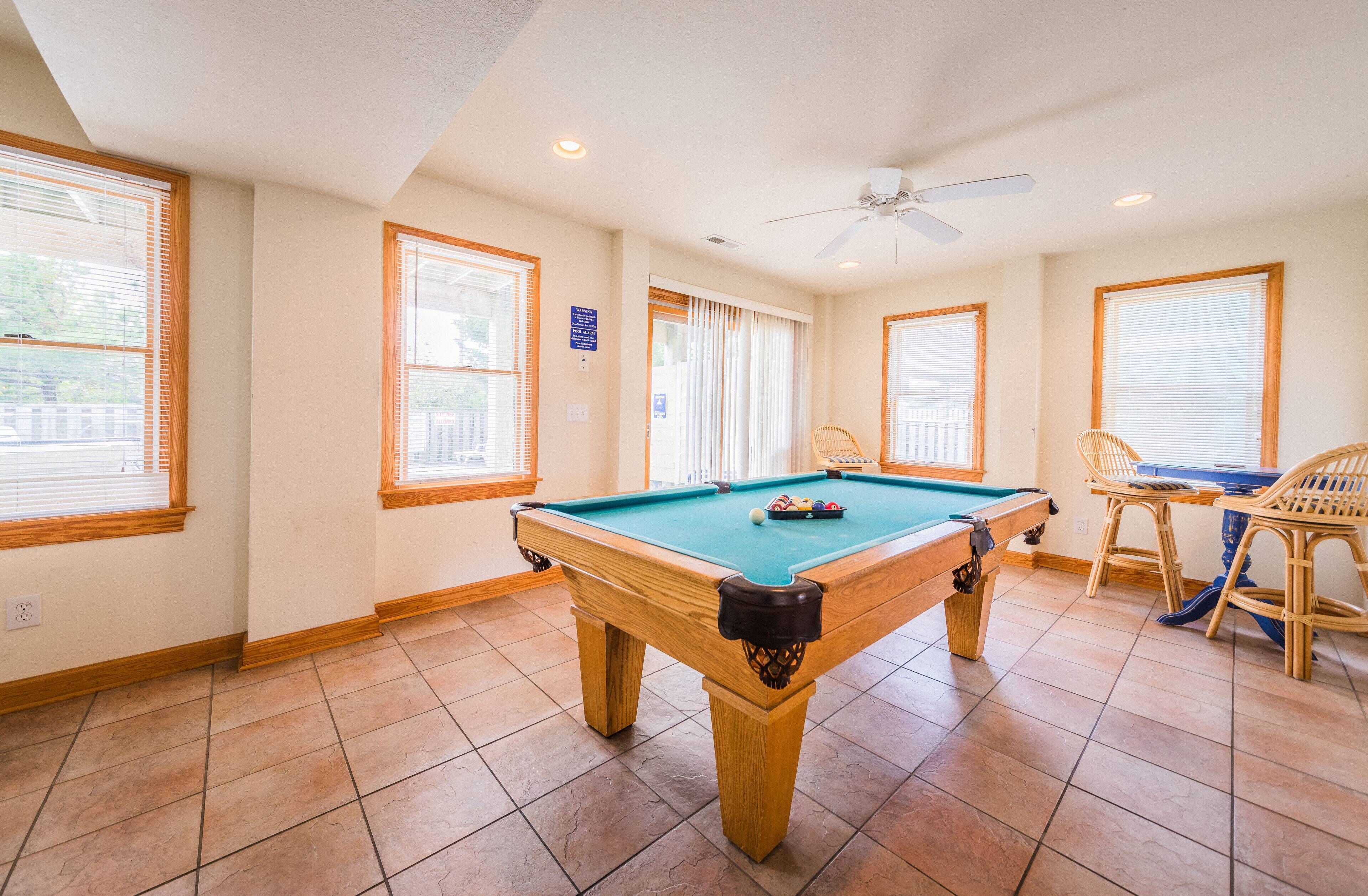 A pool table in a room with large windows, a ceiling fan, and a sign on the wall.