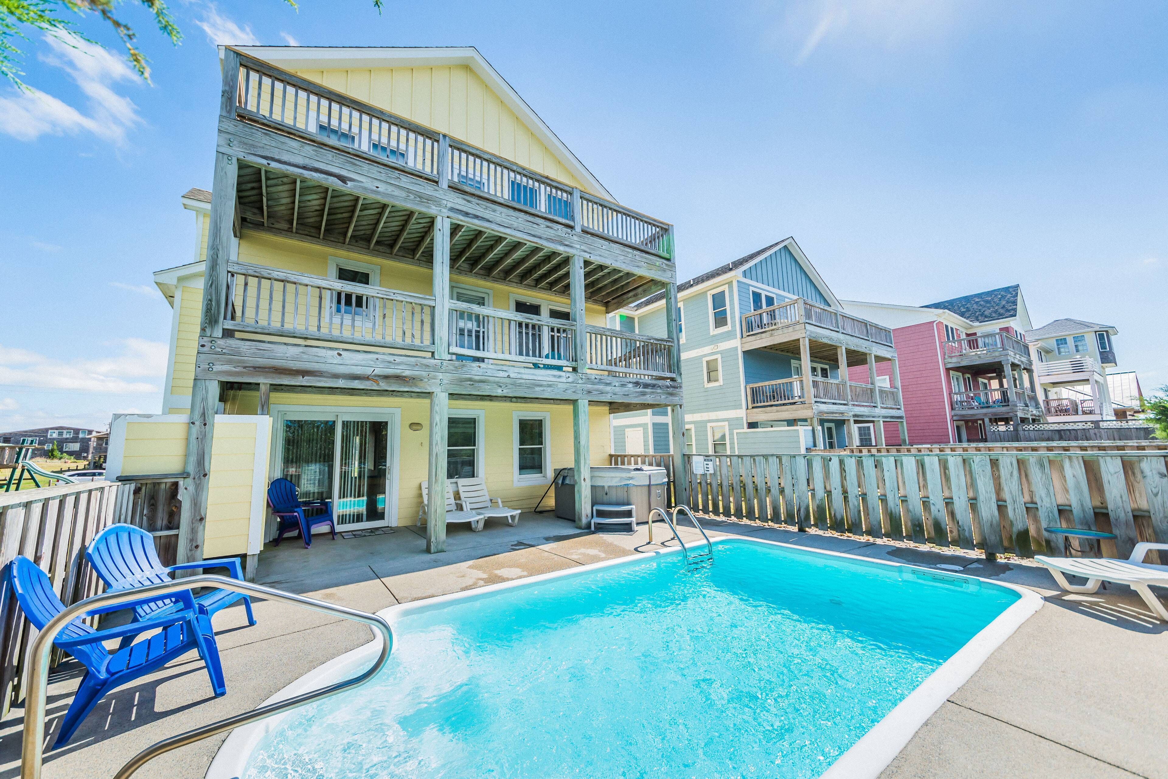 A multi-story building with a pool area, including lounge chairs and a hot tub.