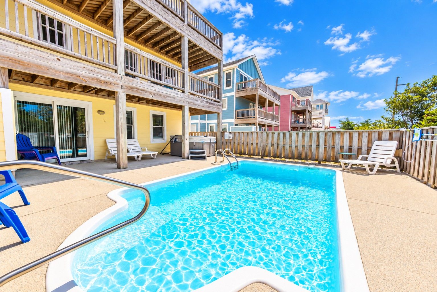 A swimming pool with a wooden deck, lounge chairs, and a wooden fence.