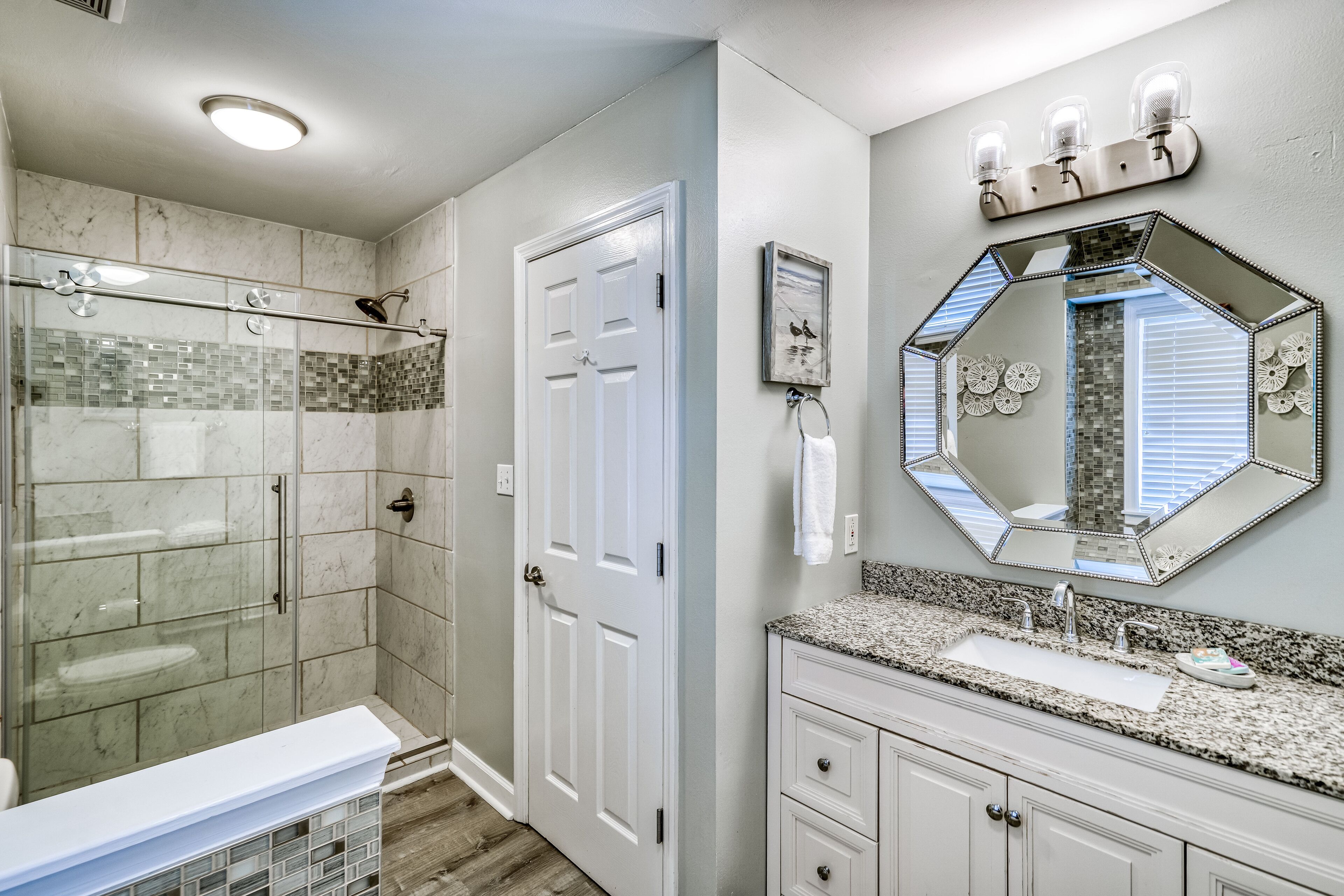 A bathroom with a glass-enclosed shower, a white vanity with a large mirror, and a sink.