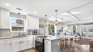 A modern kitchen with white cabinets, a large island, and pendant lighting. - The Sandpiper Crystal Beach*Pool*FirePit*BeachSvc (Destin)
