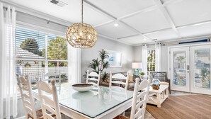 A dining area with a glass table, white chairs, a woven pendant light, and a view of the outdoors. - The Sandpiper Crystal Beach*Pool*FirePit*BeachSvc (Destin)