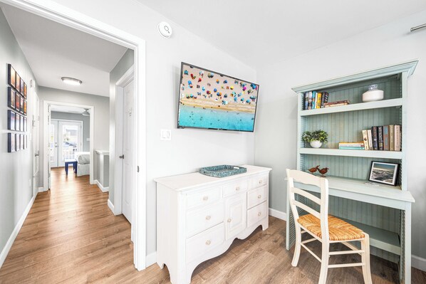 A hallway with a white dresser, a chair, and a bookshelf with books and decorative items. - The Sandpiper Crystal Beach*Pool*FirePit*BeachSvc (Destin)