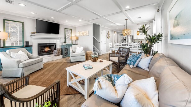 A spacious living room with a fireplace, a television, and a dining area with a chandelier. - The Sandpiper Crystal Beach*Pool*FirePit*BeachSvc (Destin)