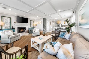 A spacious living room with a fireplace, a television, and a dining area with a chandelier. - The Sandpiper Crystal Beach*Pool*FirePit*BeachSvc (Destin)