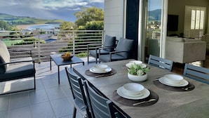 Ein Balkon mit Esstisch für vier Personen, Stühlen und Blick auf das Meer und die Hügel.