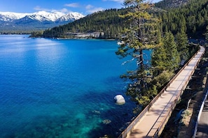 A coastal landscape with a clear blue lake, a wooden walkway, and snow-capped mountains in the background. - 4BR Incline Village Mountain Home w/ Fireplace (Incline Village)