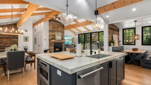 A modern kitchen with a large island, wooden beams, and a fireplace.