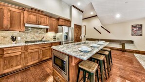 Cocina moderna con armarios de madera, encimeras de granito, electrodomésticos de acero inoxidable y una zona de bar con taburetes.