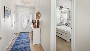 Un pasillo con alfombra azul que conduce a un dormitorio con cama, ventilador de techo y mesita de noche con lámpara.