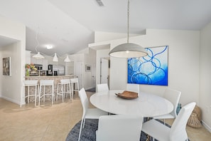 Une cuisine moderne avec des meubles blancs, un îlot central et un coin repas comprenant une table ronde et des chaises blanches.