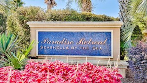 Un letrero para Paradise Retreat con un diseño de mosaico y el texto que dice "SEASHELLS BY THE SEA".