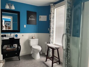 A bathroom with a blue wall, white fixtures, a black vanity, a toilet, and a shower curtain. - The York House (Fort Erie)