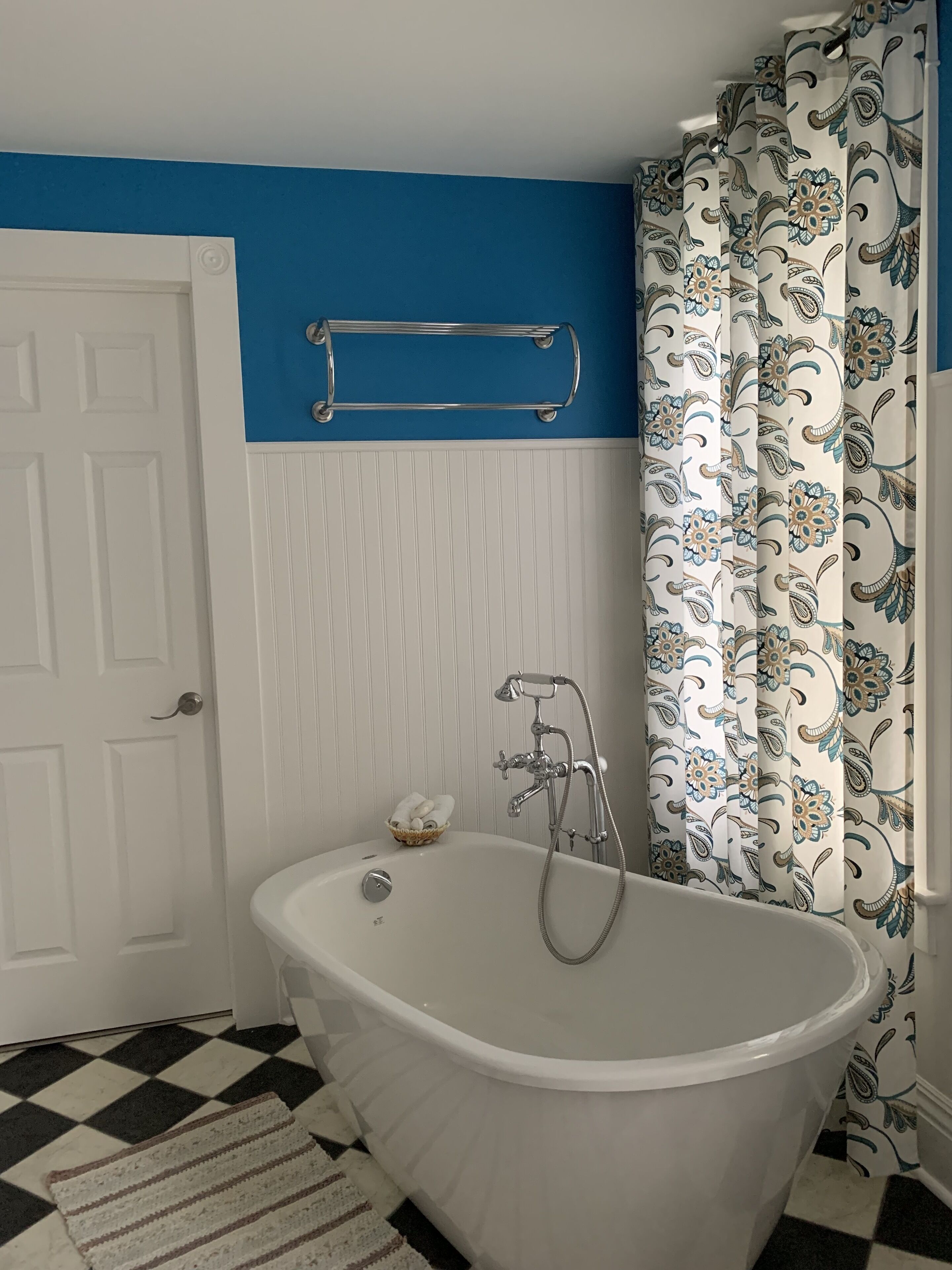 A bathroom with a freestanding bathtub, a towel rack, a door, and patterned curtains.