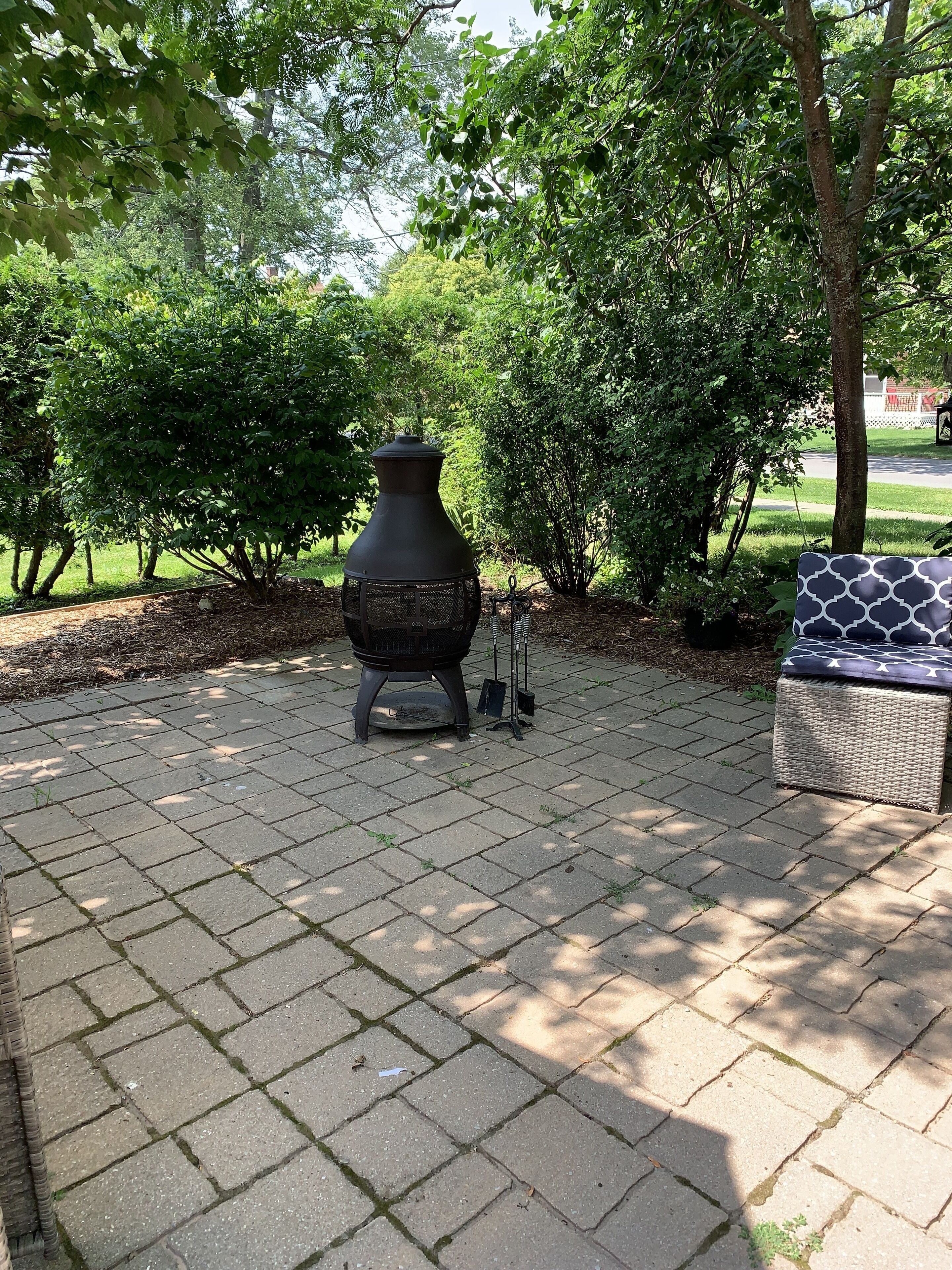 A patio area with a large black grill, a wicker bench, and a small table with a metal stand.