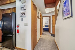 A hallway with a black refrigerator, wooden cabinets, a fire extinguisher, and a framed picture on the wall.