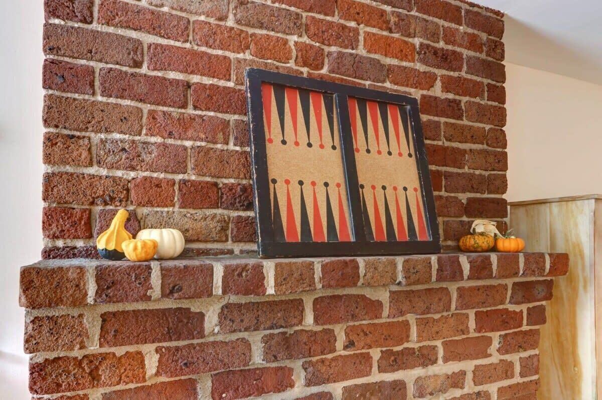 A brick fireplace with a framed board game and decorative pumpkins.