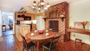 A kitchen with a brick fireplace, wooden cabinets, a dining table with chairs, and a chandelier. - Charming 1800s Garden Apt. | Dog Friendly + Garage (Savannah)