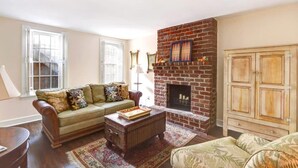 A living room with a brick fireplace, a sofa, a coffee table, and a cabinet. - Charming 1800s Garden Apt. | Dog Friendly + Garage (Savannah)