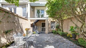 A courtyard with a table and chairs, a staircase, and a building with windows and a door. - Charming 1800s Garden Apt. | Dog Friendly + Garage (Savannah)