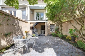 A courtyard with a table and chairs, a staircase, and a potted plant. - Charming 1800s Garden Apt. | Dog Friendly + Garage (Savannah)