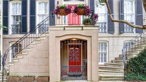 A building with a red door, a staircase, and a balcony with hanging planters. - Charming 1800s Garden Apt. | Dog Friendly + Garage (Savannah)