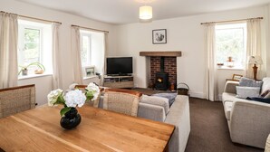 A living room with a fireplace, a television, a dining table with a vase of flowers, and a sofa. - Hilber Cottage (Ambleside)