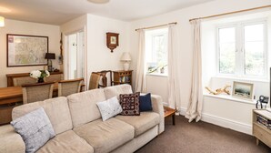 A living room with a beige sofa, a wooden coffee table, a map on the wall, and a window with curtains. - Hilber Cottage (Ambleside)
