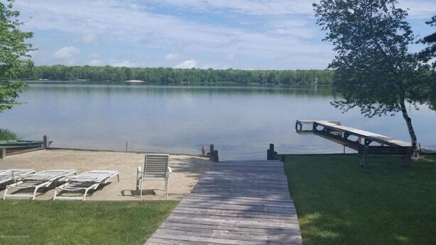 A wooden dock leading to a sandy beach with lounge chairs and a bench. - Spacious Mountain Home with Fireplace, Game Room in Bear Creek Lake Community! (Jim Thorpe)