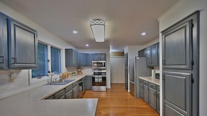 A modern kitchen with grey cabinets, stainless steel appliances, and a wooden floor. - Spacious Mountain Home with Fireplace, Game Room in Bear Creek Lake Community! (Jim Thorpe)